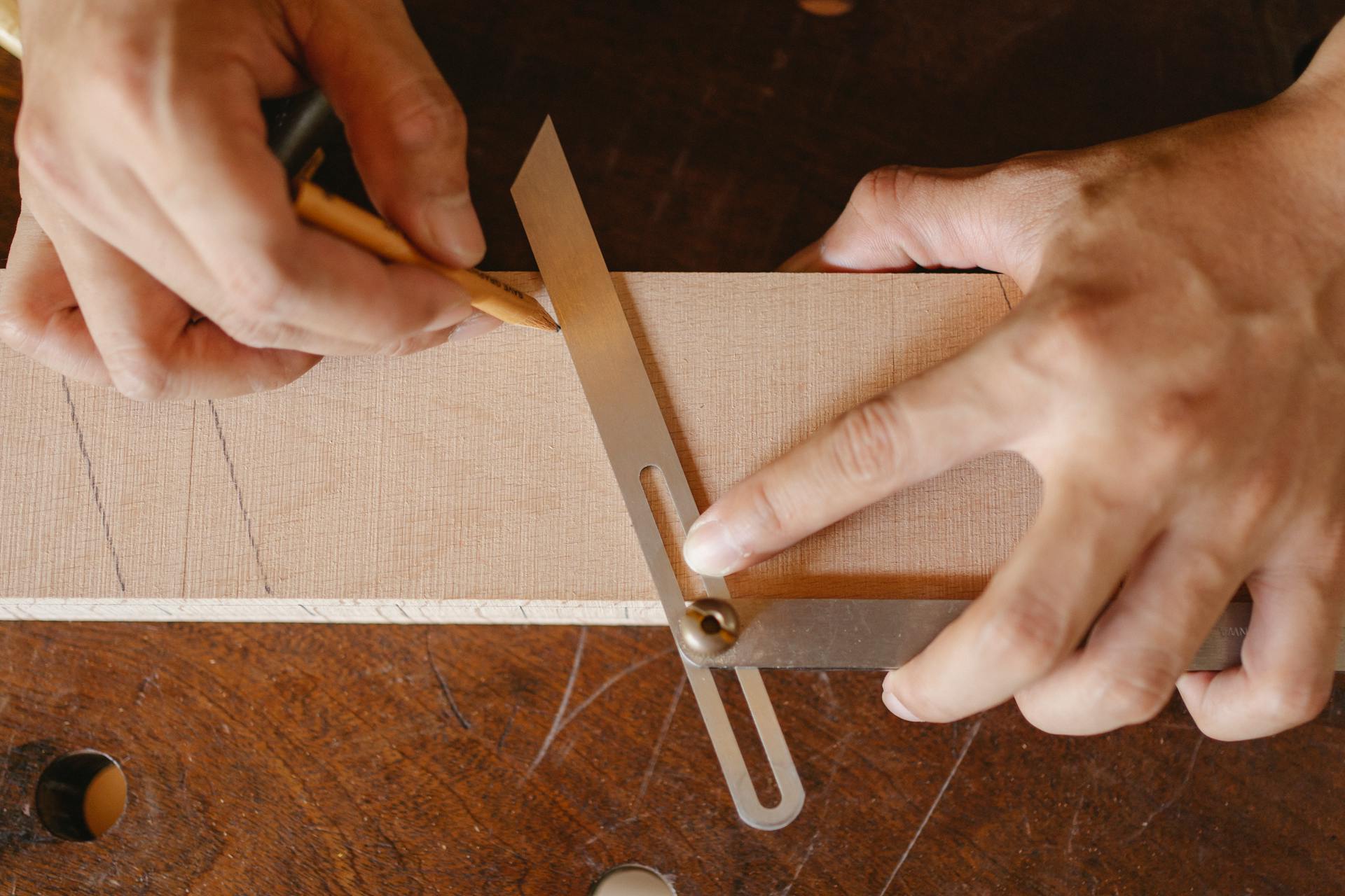 Top view of crop anonymous woodworker drawing diagonal line on wooden block using bevel on workbench