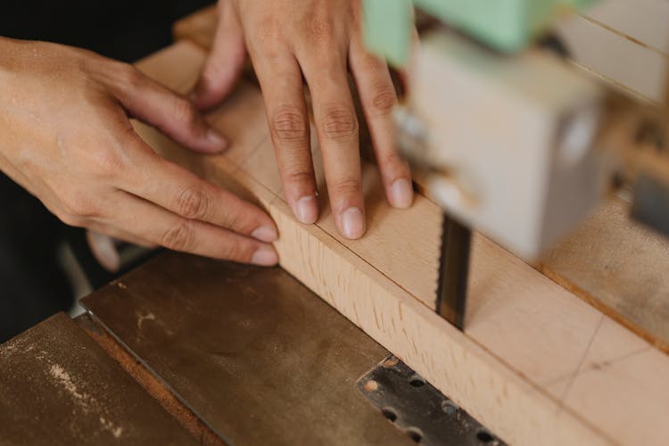 Faceless Artisan Cutting Wooden Plank Using Band Saw In Workroom