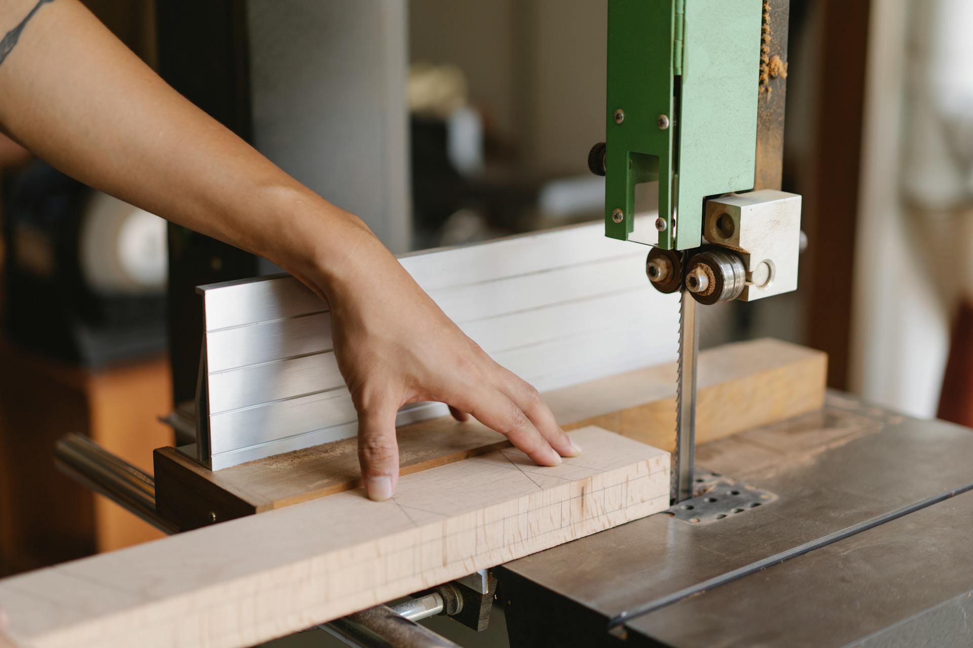 Crop anonymous artisan cutting wooden plank using electric equipment with sharp blade on table