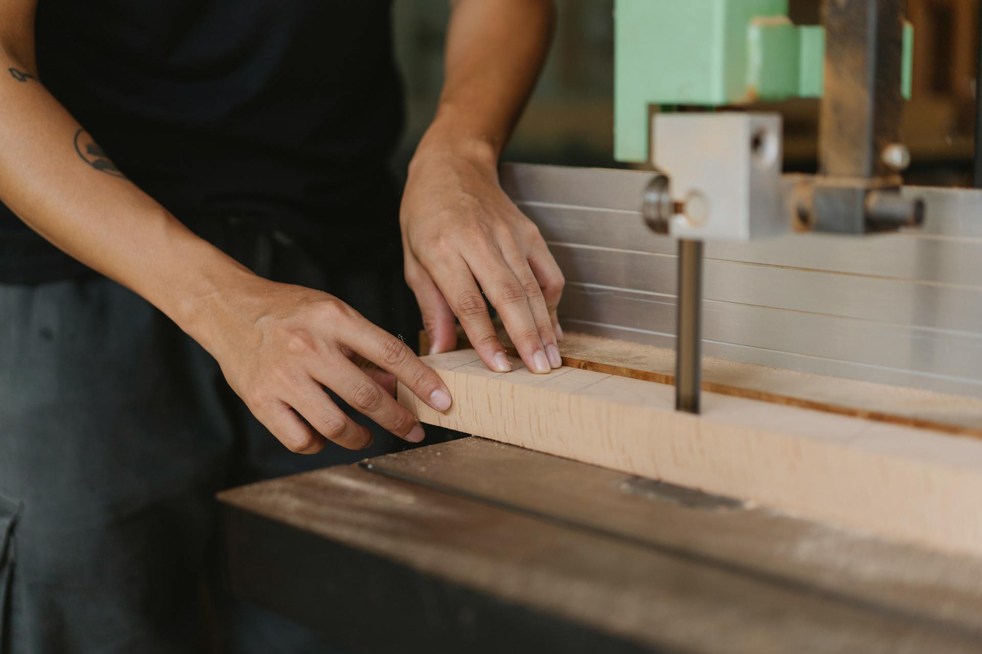 Crop anonymous male joiner sawing wooden block with electric machine on table in workroom