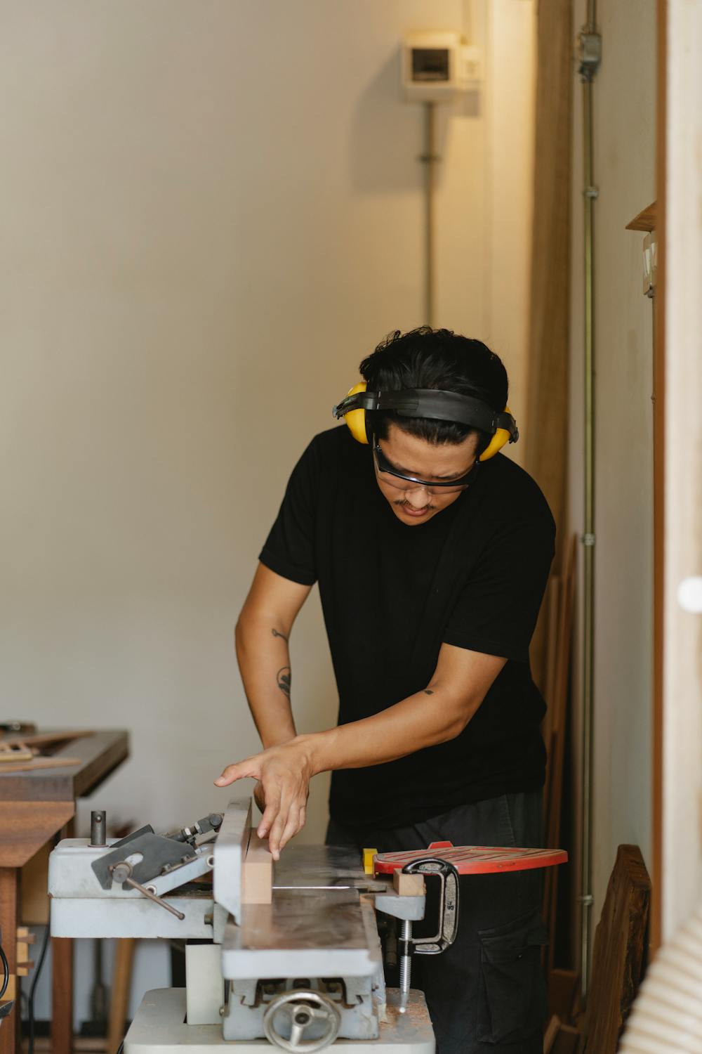 Concentrated Asian carpenter leveling lumber on jointer in workshop ...
