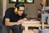 Attentive Asian joiner leveling timber on planer in workshop
