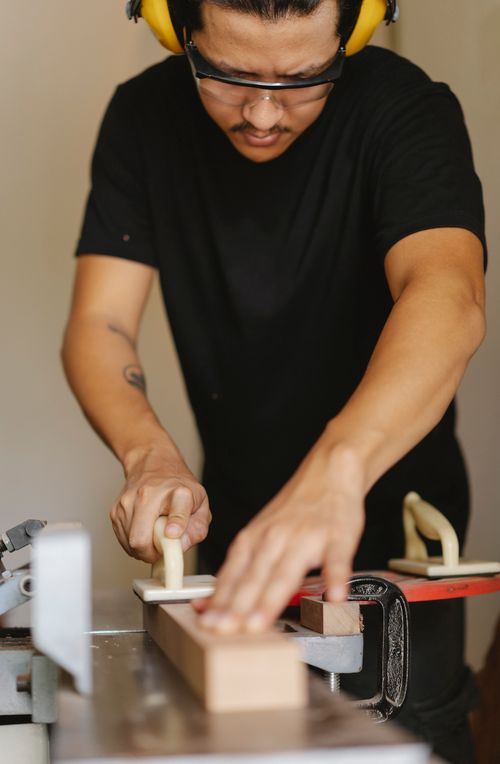Free Crop attentive ethnic male joiner in protective glasses flattening wooden plank on carpentry machine using manual instrument Stock Photo