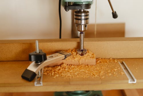 Electric drill press making hole in timber plank fixed with carpenter vice on workshop table