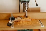 Electric drill press making hole in timber plank fixed with carpenter vice on workshop table