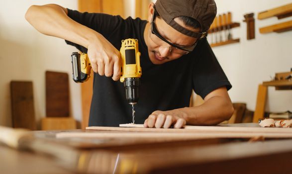Crop professional carpenter drilling holes while preparing wooden details for work in workshop