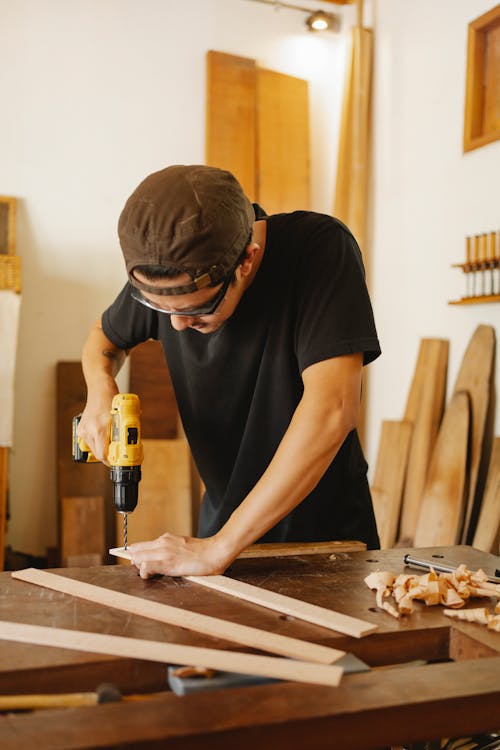 Skilled man drilling wooden planks on workbench