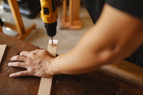 Crop man drilling hole in wooden board