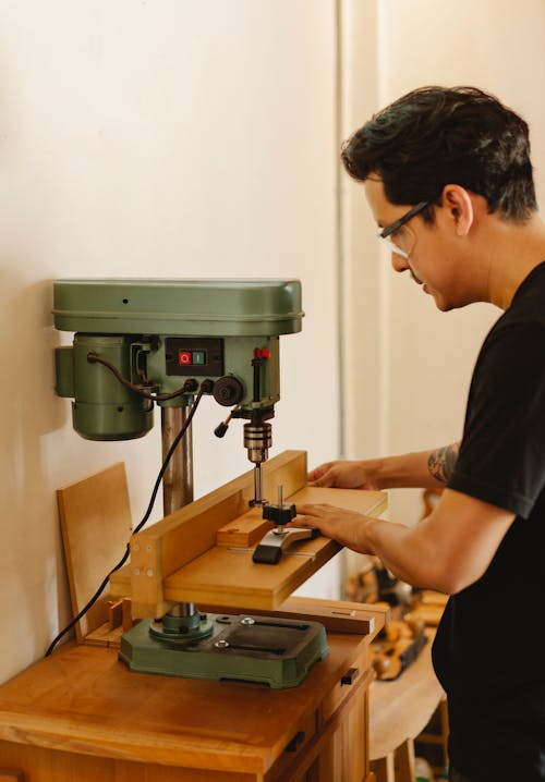 Craftsman drilling hole with drill press in workshop