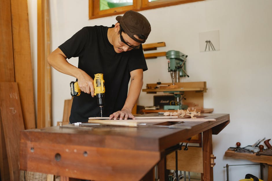 Focused man in cap standing near workbench and drilling hole in plank while repairing wooden detail