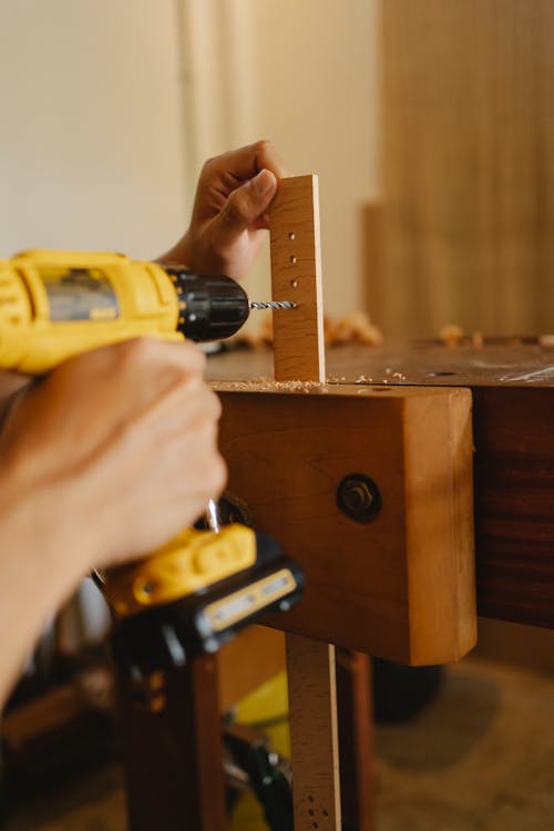 Crop anonymous skillful male using screwdriver while drilling holes in timber detail in workshop