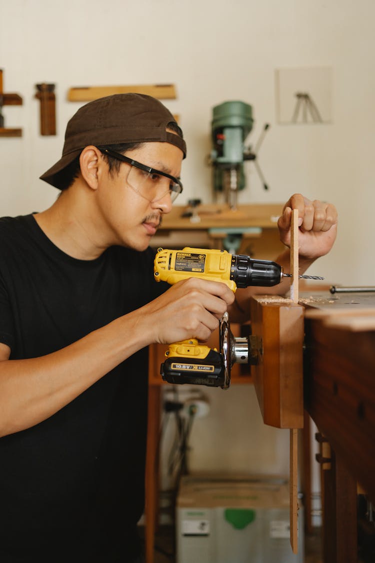 Ethnic Man In Safety Glasses Drilling Wooden Plank