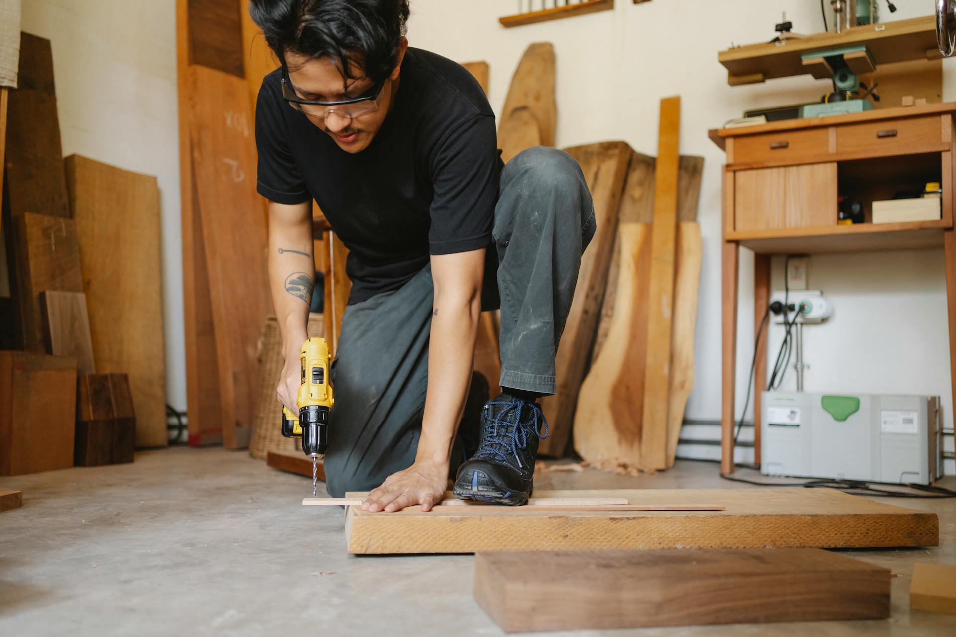 Ethnic man leaning on wooden plank and drilling hole