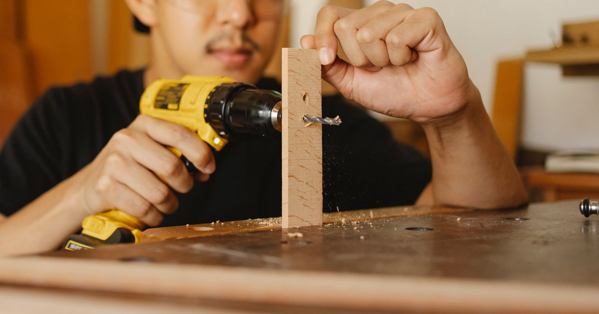A man drilling a hole in a strip of wood with a cordless drill