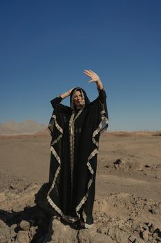 一位身着传统黑色长袍的女子，在干旱的沙漠中优雅地摆着姿势