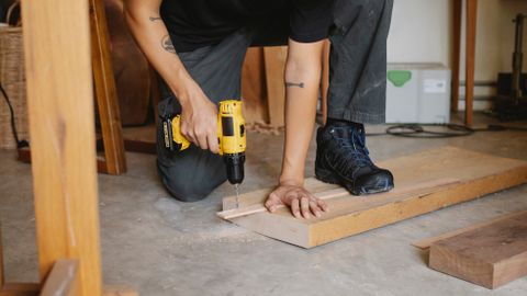 Crop anonymous male drilling piece of timber detail with screwdriver among lumber in workshop