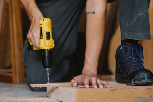 Crop anonymous male drilling and pressing timber detail with foot in boot in workshop