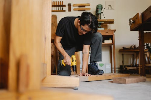 Free Pensive male drilling wooden surface of plank in workshop with equipment for carpentry Stock Photo