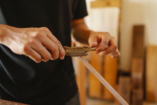 Crop joiner using sharp drawknife while forming think hardwood plank in light joinery on blurred background