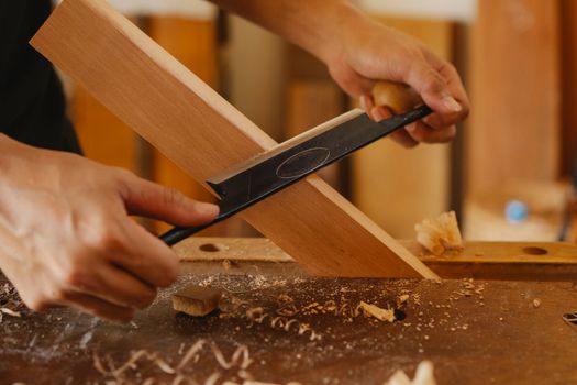 Male artisan shaping plank with drawknife