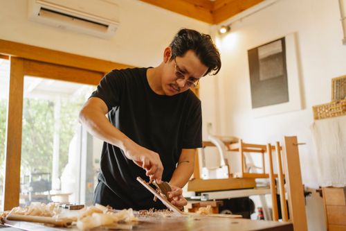 Free From below of Asian joiner shaping wooden plank with carpentry tool during work in workshop Stock Photo