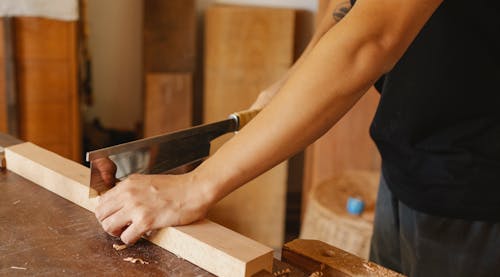 Professional woodworker cutting wood with hacksaw