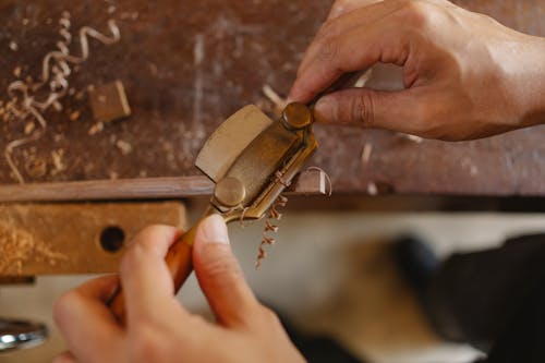 High angle of crop carpenter carving wooden detail with router plane while working at workbench in joinery workshop