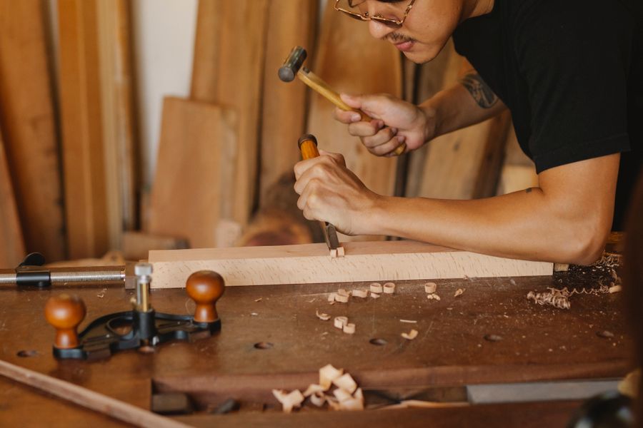 A maker tapping a chisel with a mallet at a worn workbench