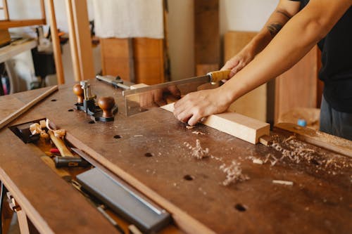 Woodworker cutting wooden plank with hacksaw