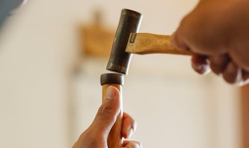 Low angle of crop anonymous craftsman hammering instrument while working in joinery workshop