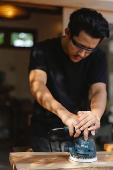 在光线充足的车间里，木匠专注地用电动砂光机打磨木头