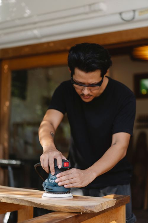 Free Serious craftsman in protective glasses creating wooden plank with sander while working in joinery Stock Photo