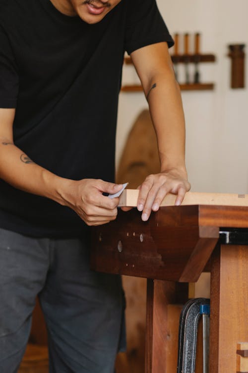 Unrecognizable craftsman in casual clothes polishing wooden detail while working in professional workshop