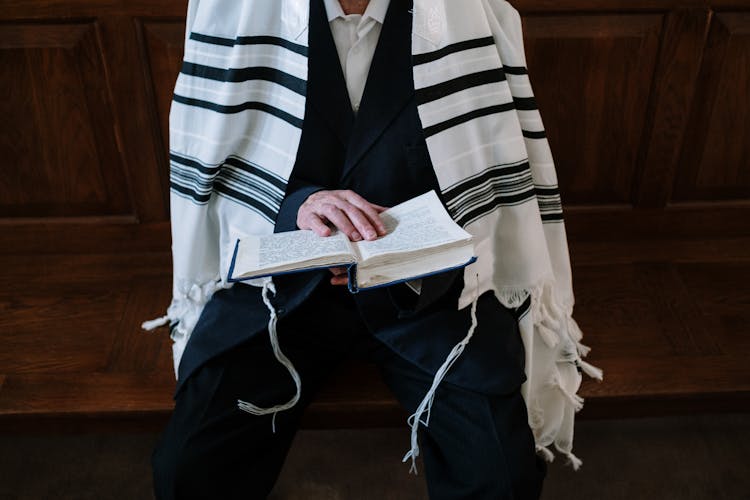 A Person In A Tallit Reading A Chumash