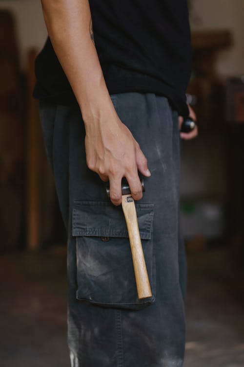 Side view of unrecognizable craftsman in casual clothes standing with hammer in workshop
