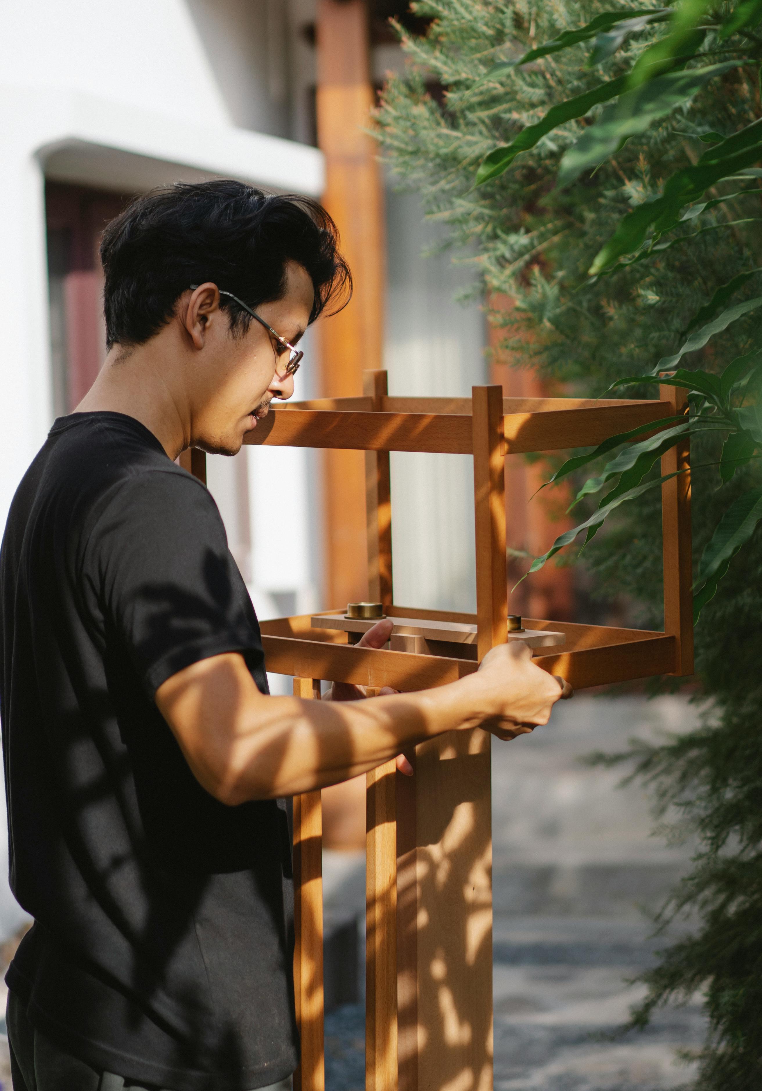 Side view of focused young male joiner in eyeglasses and casual outfit creating wooden bird table