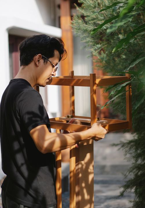 Free Side view of focused young male joiner in eyeglasses and casual outfit creating wooden bird table Stock Photo