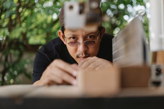 Concentrated ethnic craftsman in casual wear in hat and eyeglasses working on workbench with wood plank outside near workshop at daytime