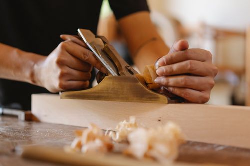 Free Crop faceless male carpenter shaping wooden board using jack plane during work in studio Stock Photo