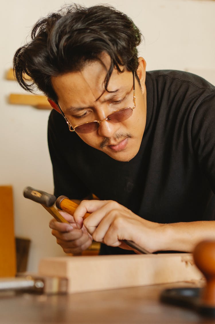 Serious Young Ethnic Male Woodworker Working With Chisel And Hammer In Joinery