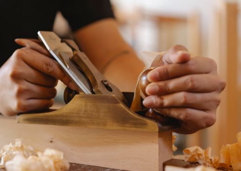 Faceless man flattening lumber board with hand plane in joinery
