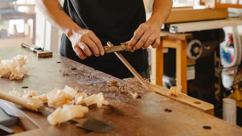 Free Crop anonymous male carpenter smoothing wooden stick with spokeshave standing at workbench in studio on sunny day Stock Photo