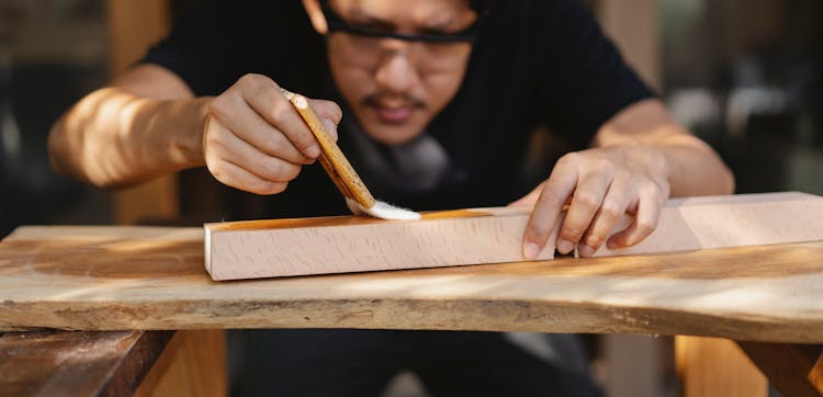 Concentrated Young Ethnic Master Varnishing Wooden Detail In Workshop