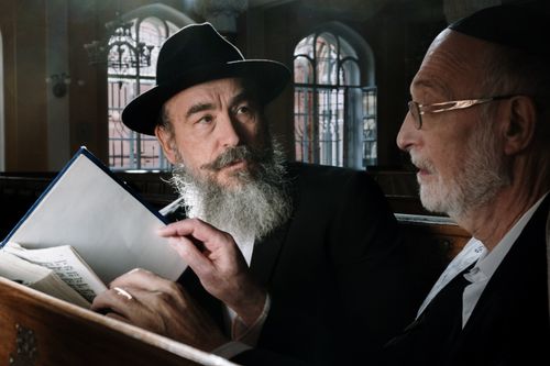 Free Two senior men engaging in a thoughtful conversation while reading religious texts inside a synagogue. Stock Photo