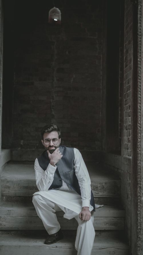 Free A fashionable man with a beard and glasses sitting on rustic steps, exuding a modern and cultural vibe. Stock Photo