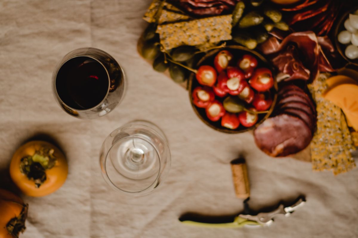 Glass of red wine next to a board of cured meats, stuffed peppers and olives for a Hispanic Heritage Month gathering
