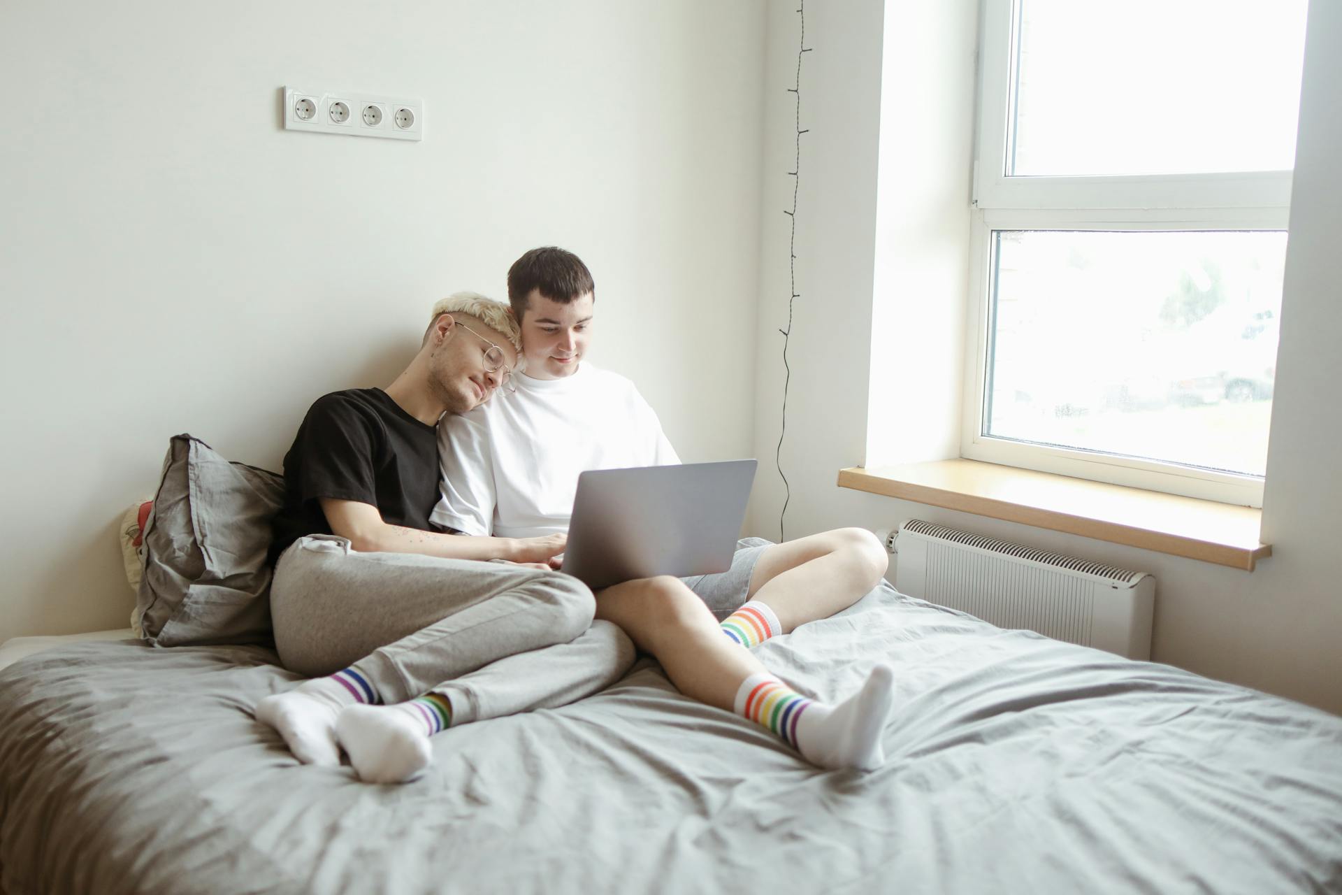 Two adult men enjoying quality time together in a bedroom, sharing a laptop.