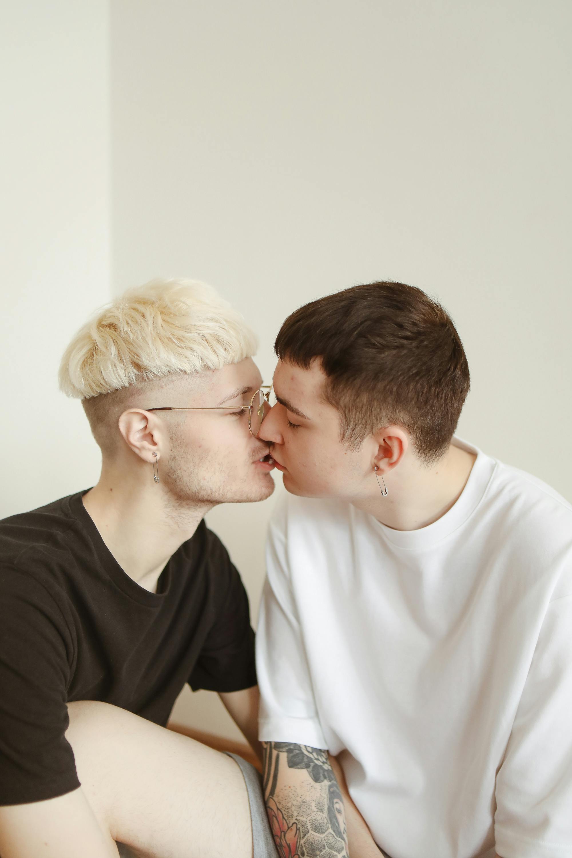 man in a black shirt with blond hair and a man in white shirt kissing