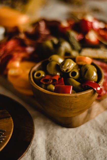 A small bowl of bright grass-green Castelvetrano olives with a few pits and a jar of brine in the background.