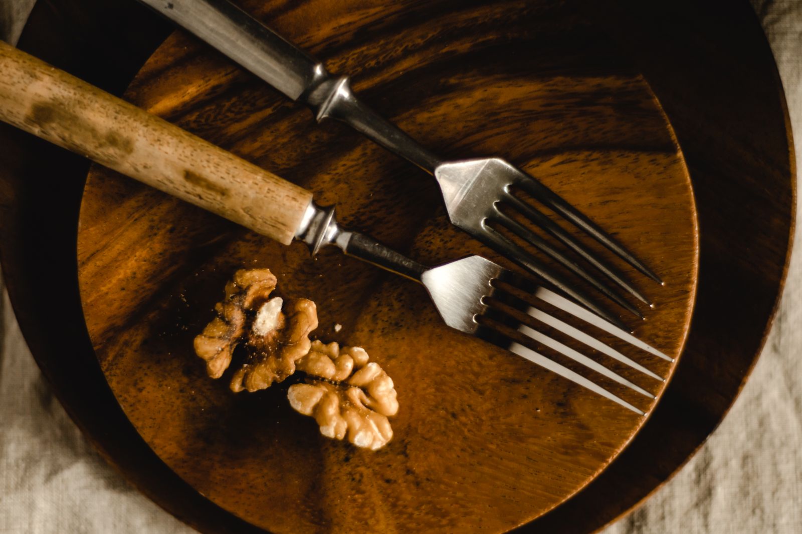 A close-up of forks and walnuts on a rustic wooden plate, showcasing a simple still life.